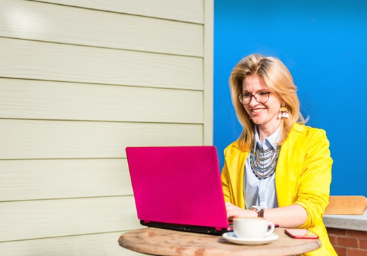 A woman wearing a yellow blazer uses her laptop at a coffee shop to log a complaint online. 