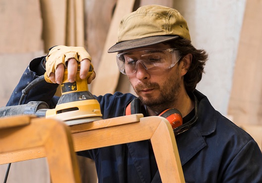 A male woodworker operates a machine to sand wooden furniture.