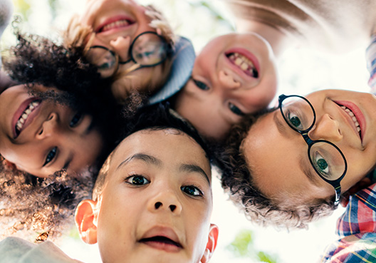 Several young kids smile while looking down at a camera. 