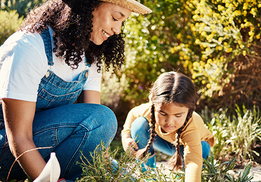 A mom wearing a straw hat works in a garden with her daughter. 